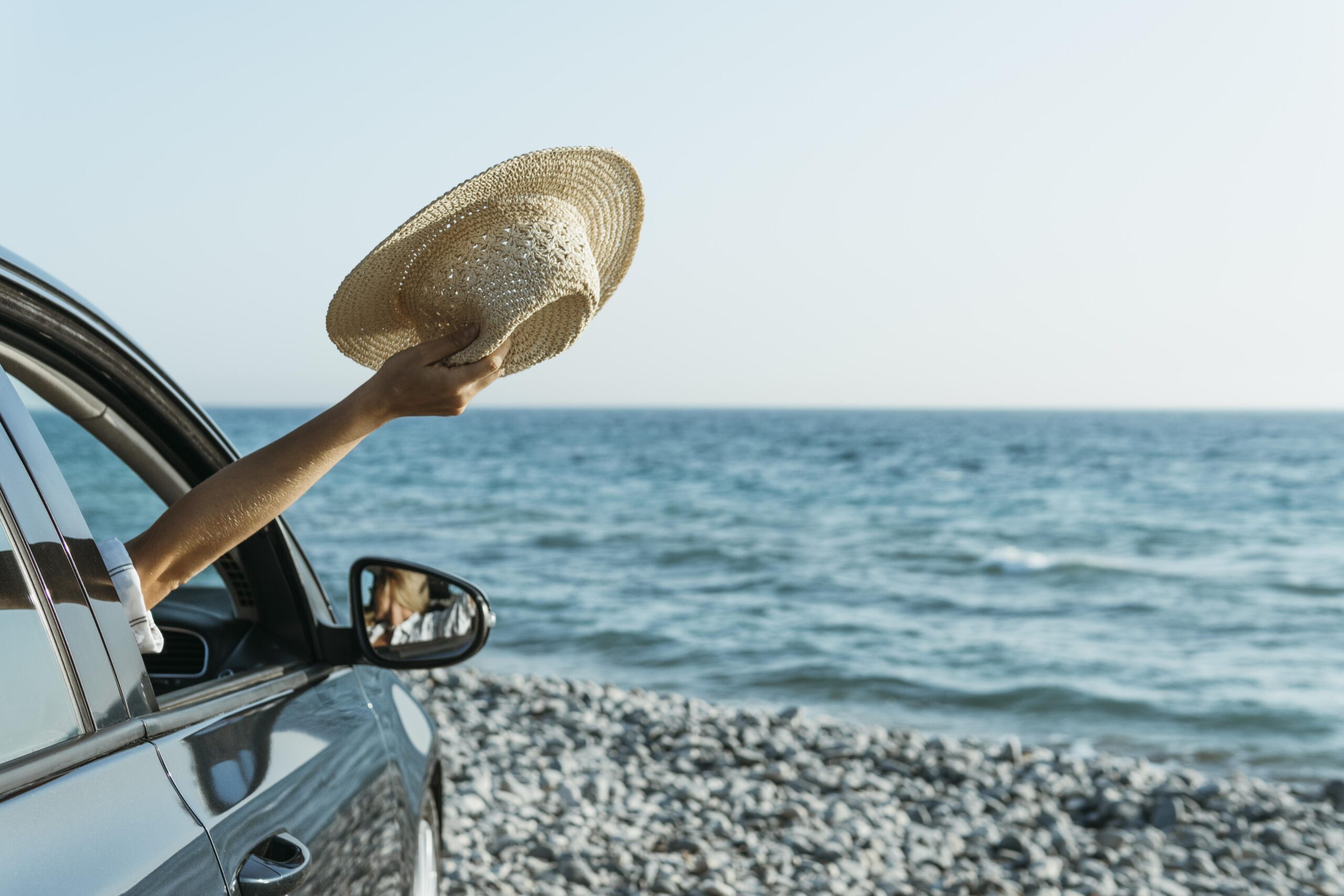 mid shot woman hand out car window holding hat near sea scaled.jpg